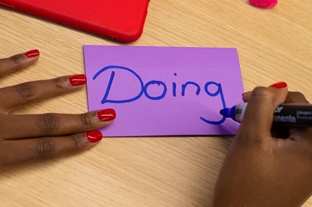 Imagem de mulher escrevendo a palavra 'doing' em papel roxo